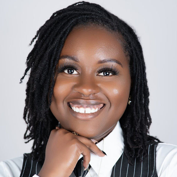 Woman with braided hair wearing a pinstripe vest over a white shirt against a plain background